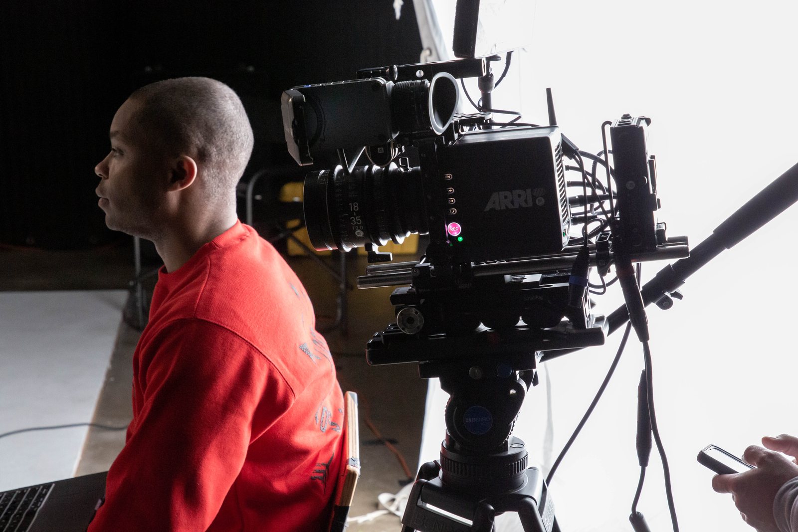 Camera operator in a red sweatshirt beside an ARRI cinema camera on a tripod