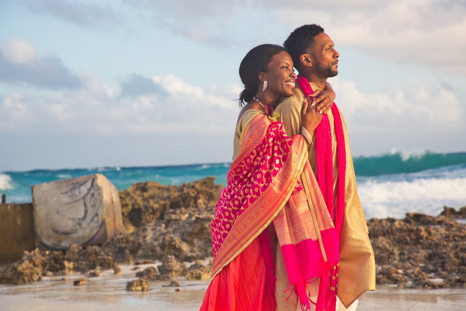 Couple embracing on a rocky beach, both looking out at the surf