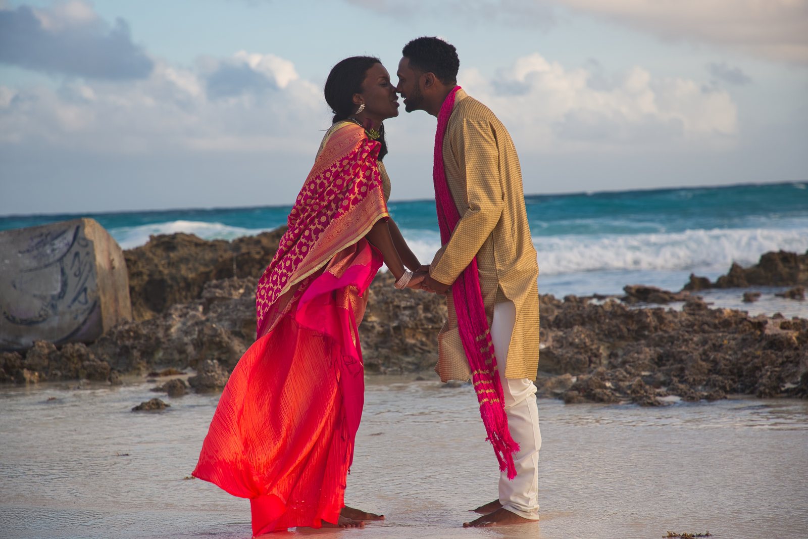 Couple kissing on a rocky beach, red sari lifted by the wind
