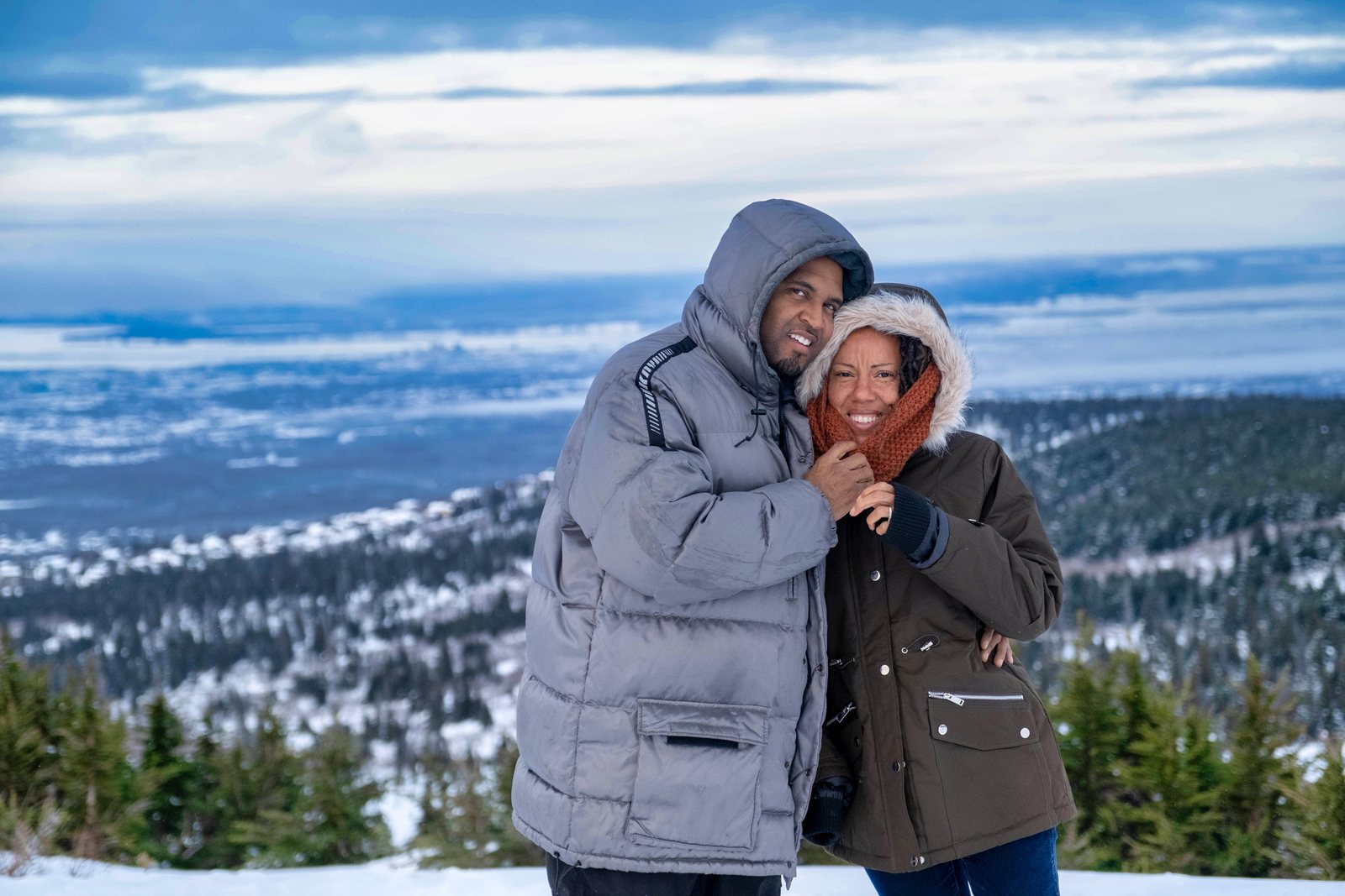 Couple in winter coats laughing at a snowy mountain overlook