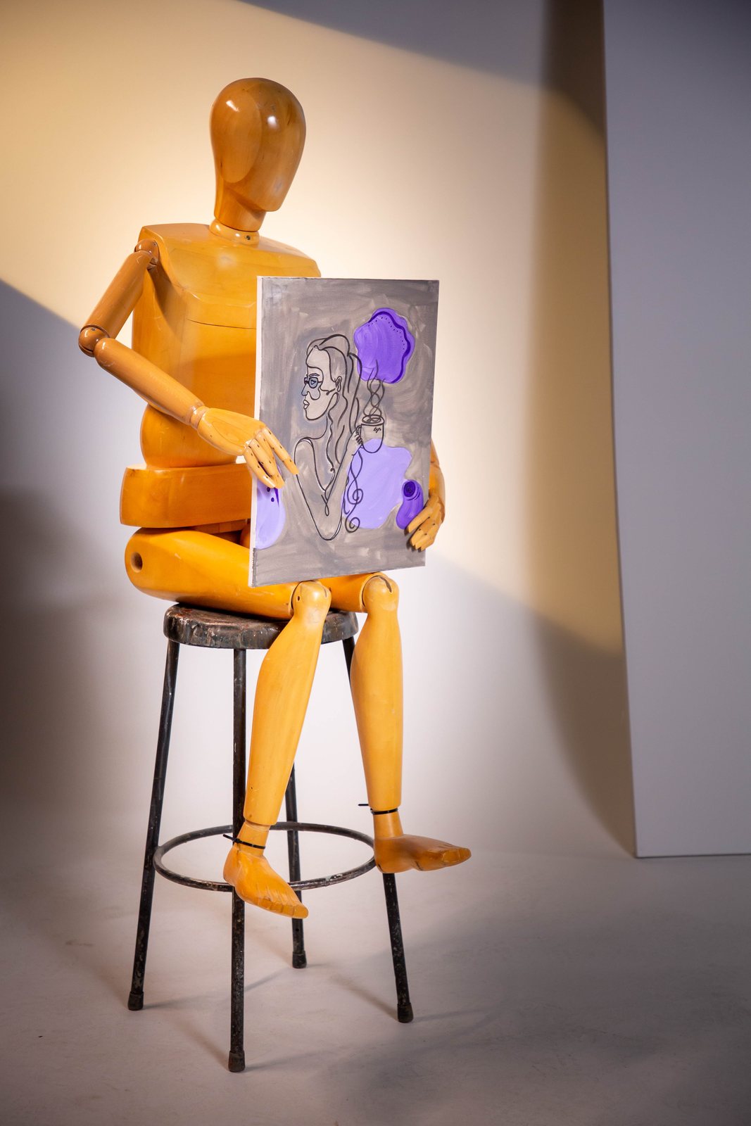 Wooden artist's mannequin on a stool holding a small painted canvas