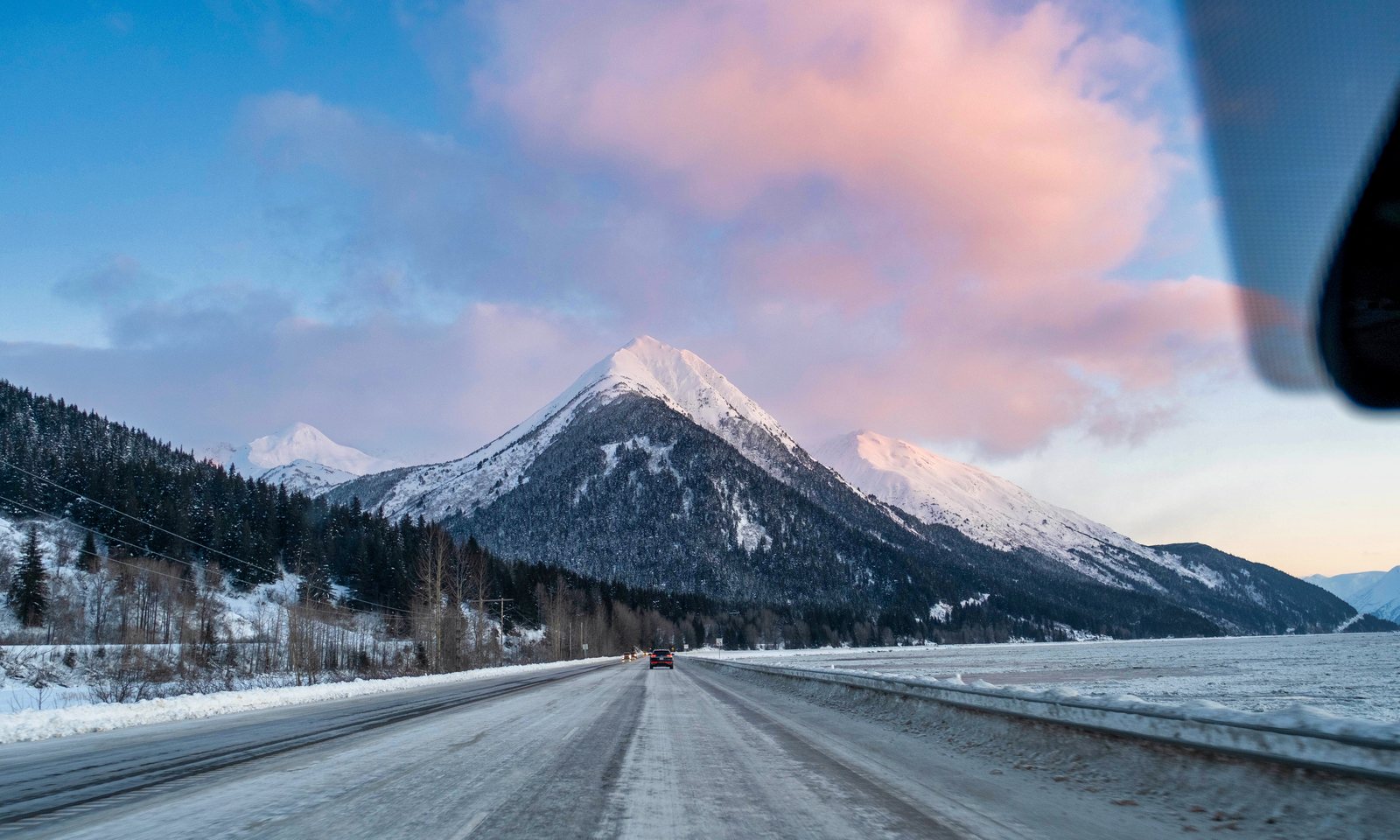Snowy highway running toward a pink-lit mountain at dusk