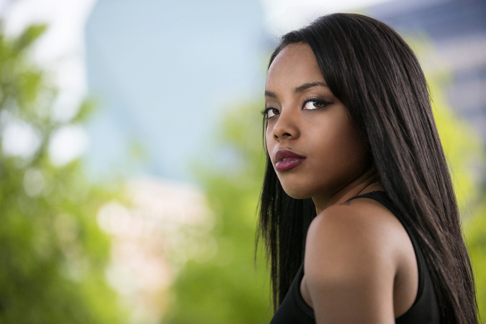 Woman in a black top looking back over her shoulder against soft green