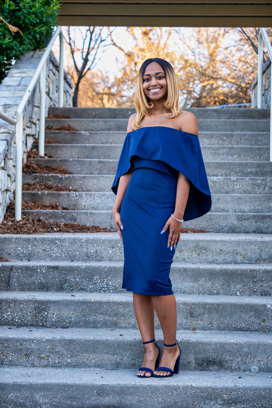 Woman in a blue off-shoulder dress on stone steps under bare trees