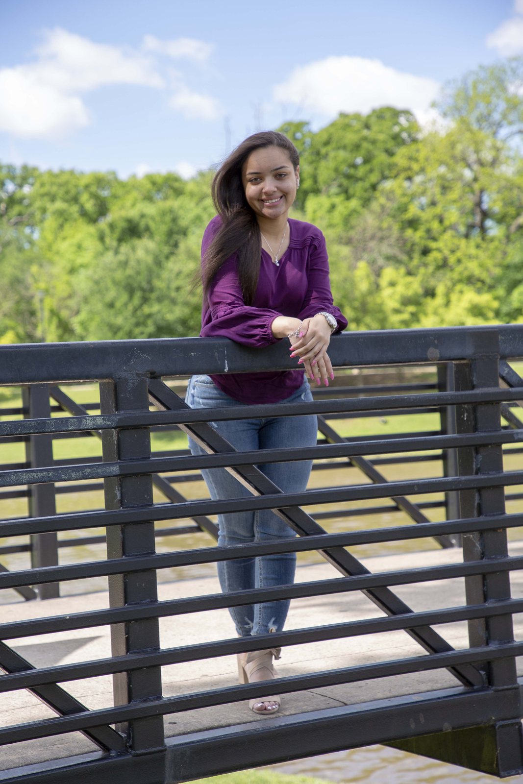 Woman in a purple blouse leaning on a bridge rail above a green park