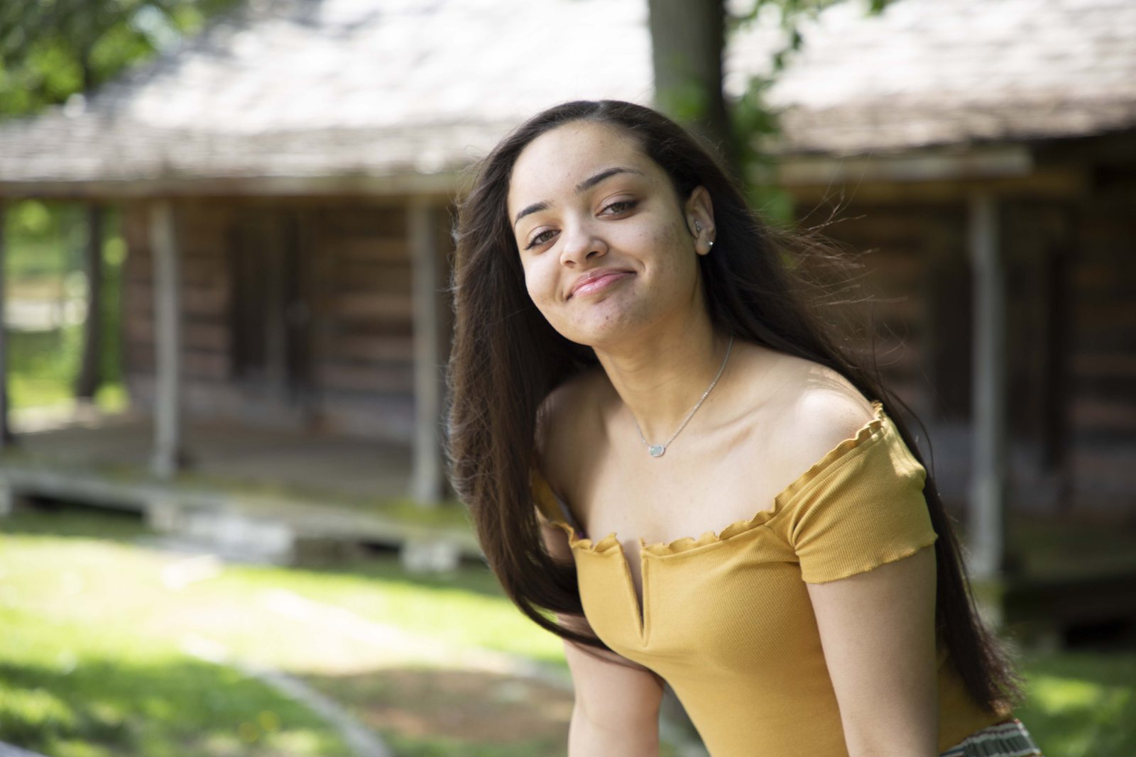 Woman in a yellow top smiling in front of a log cabin