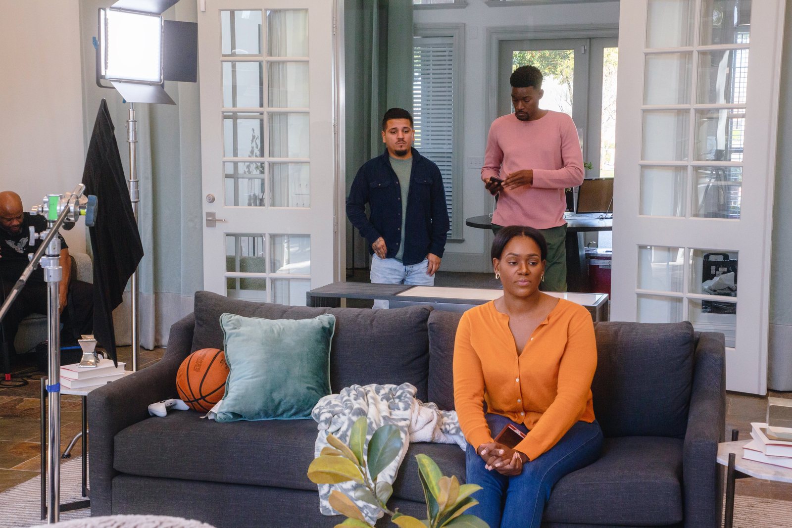Actor on a grey sofa with a basketball while the crew sets a shot