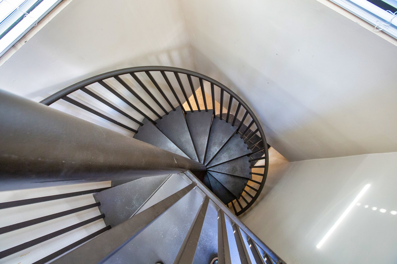 Spiral staircase seen from above, iron rail curling into a skylight