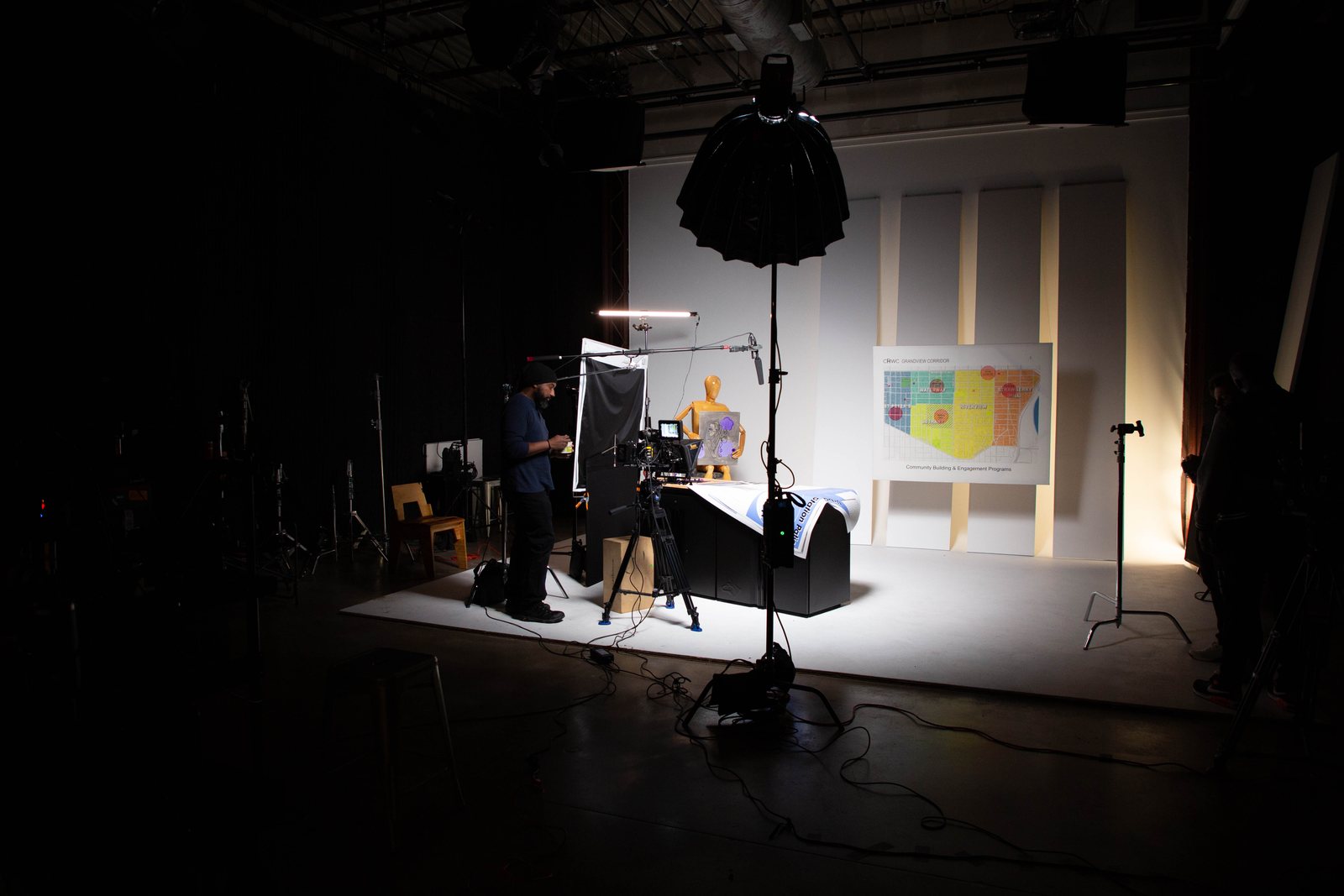 Wide view of a dark studio with one lit set and a painting on the wall