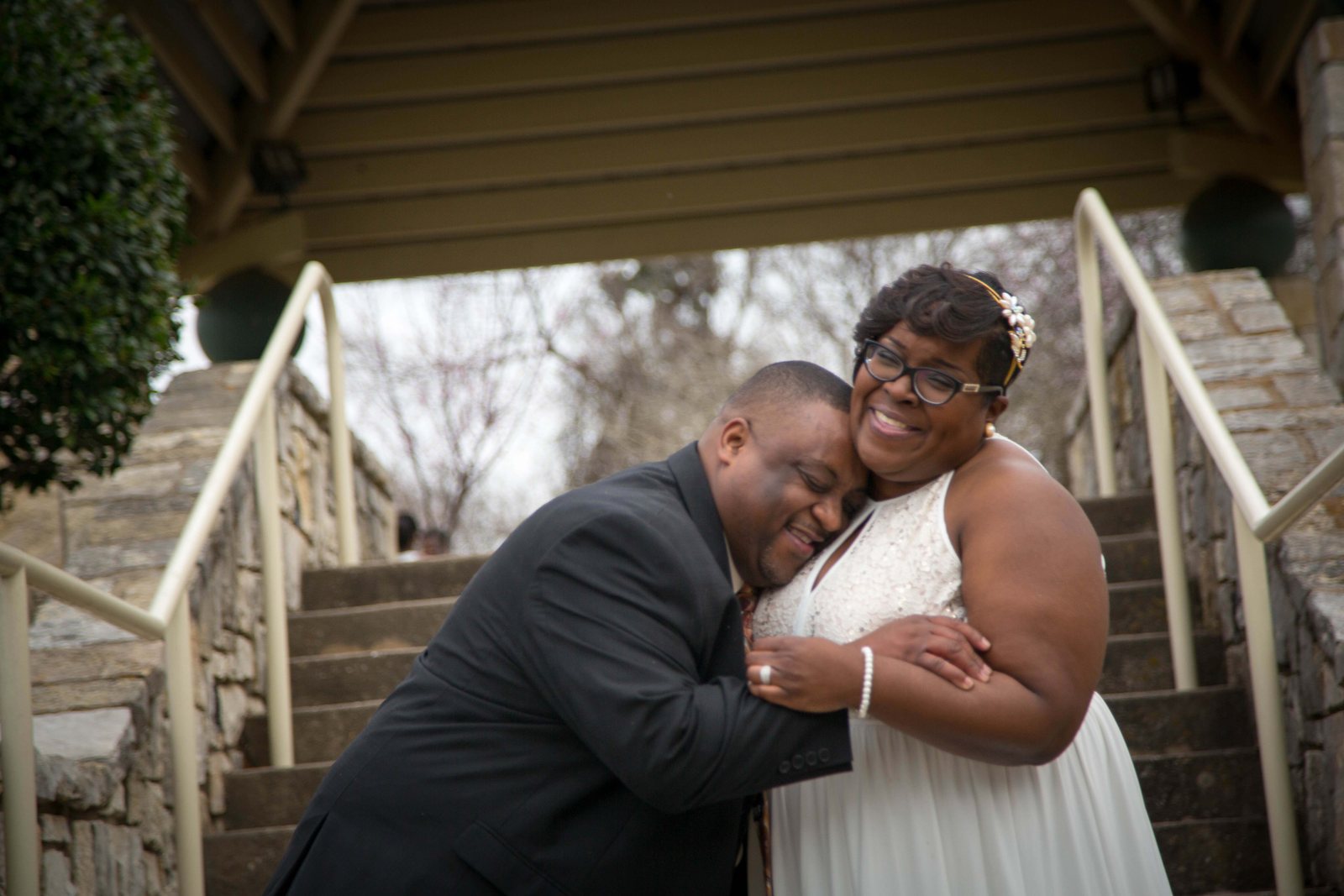 Groom hugging the bride from the side on a stone stair in the shade